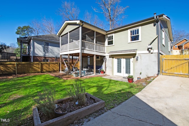 rear view of property featuring a patio area, a sunroom, french doors, and a lawn