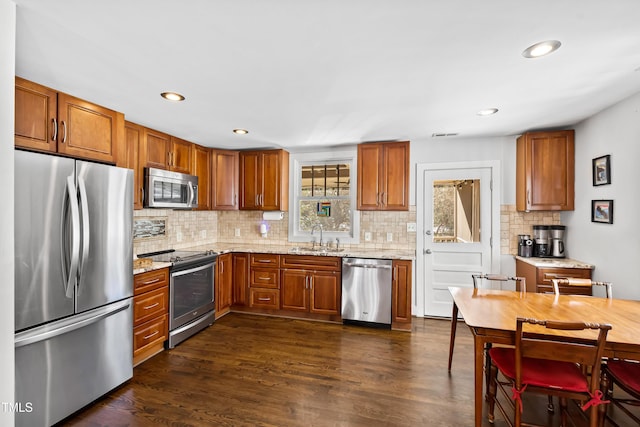 kitchen featuring sink, dark wood-type flooring, backsplash, stainless steel appliances, and light stone counters