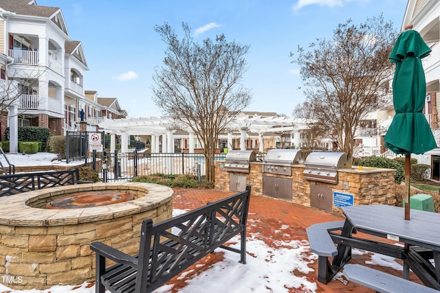 snow covered patio with an outdoor kitchen, a grill, and a pergola