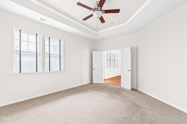 empty room featuring a raised ceiling, crown molding, light carpet, and ceiling fan