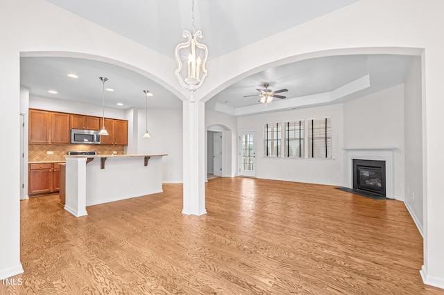 unfurnished living room featuring ceiling fan with notable chandelier, light wood-type flooring, and a tray ceiling