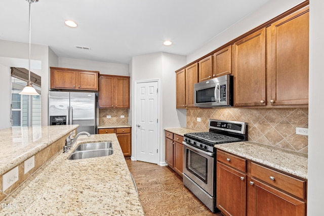 kitchen featuring pendant lighting, stainless steel appliances, sink, and light stone counters