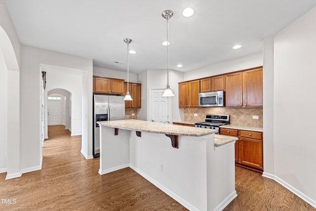 kitchen with a kitchen island, hardwood / wood-style floors, hanging light fixtures, stainless steel appliances, and light stone countertops