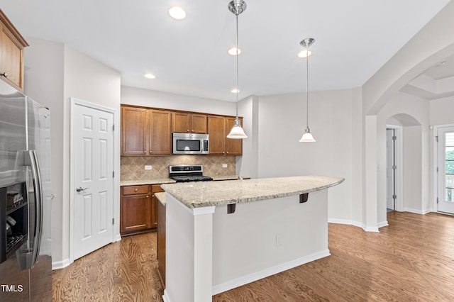 kitchen featuring a breakfast bar area, hanging light fixtures, a kitchen island with sink, stainless steel appliances, and light stone countertops