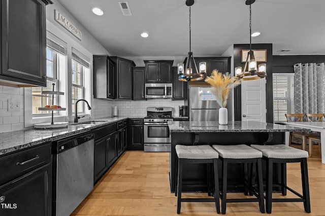 kitchen with appliances with stainless steel finishes, sink, dark stone countertops, and decorative light fixtures