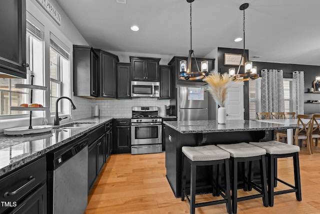 kitchen with a breakfast bar area, a center island, appliances with stainless steel finishes, pendant lighting, and dark stone counters