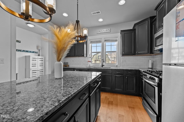 kitchen with hanging light fixtures, appliances with stainless steel finishes, light wood-type flooring, and dark stone counters