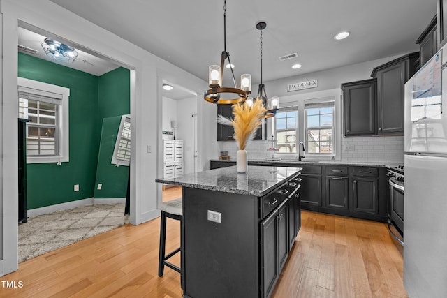 kitchen with a kitchen island, a breakfast bar, pendant lighting, sink, and stainless steel range oven