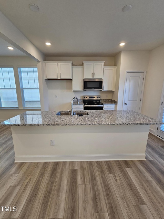 kitchen featuring appliances with stainless steel finishes, sink, white cabinets, a kitchen island with sink, and light stone countertops