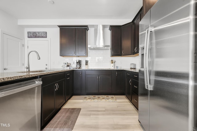 kitchen with wall chimney exhaust hood, sink, tasteful backsplash, light stone counters, and stainless steel appliances