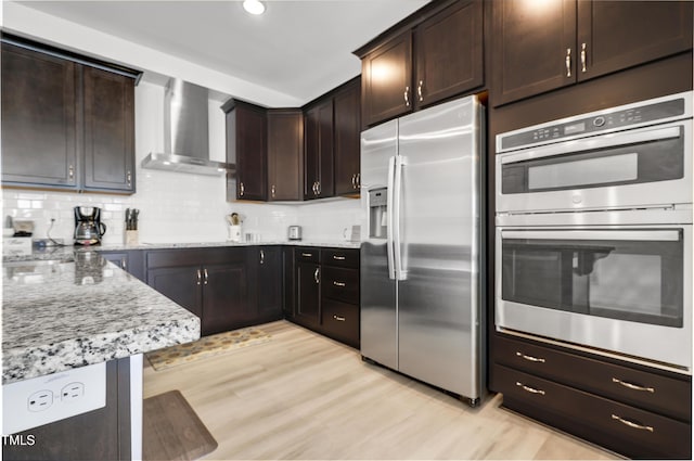 kitchen featuring stainless steel appliances, light stone countertops, dark brown cabinets, and wall chimney exhaust hood