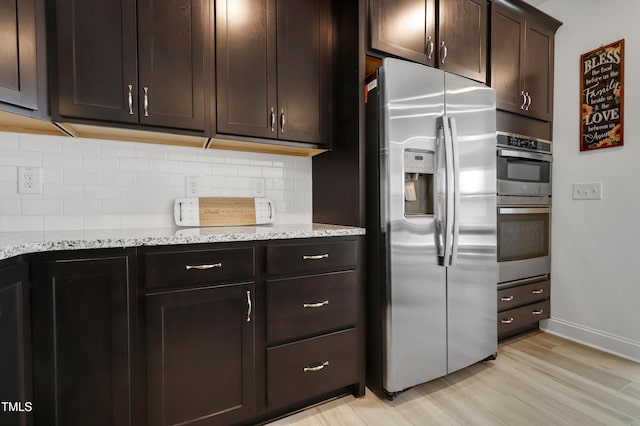 kitchen with dark brown cabinetry, appliances with stainless steel finishes, light stone countertops, light hardwood / wood-style floors, and decorative backsplash