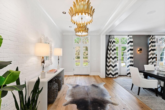 entryway featuring brick wall, light hardwood / wood-style floors, crown molding, an inviting chandelier, and french doors