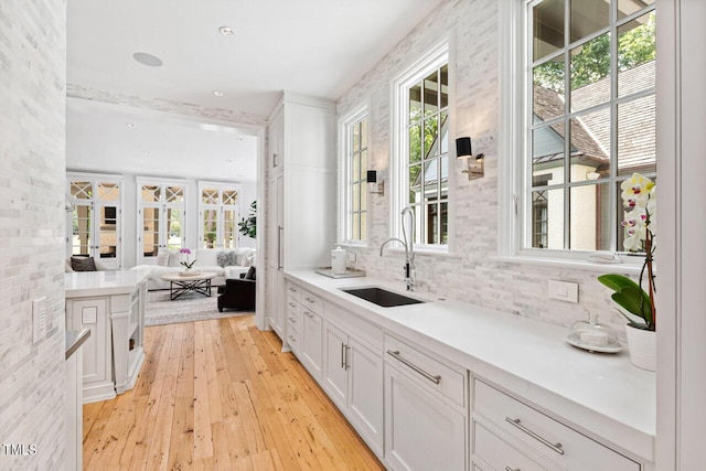 interior space featuring light hardwood / wood-style floors, sink, decorative backsplash, and white cabinets