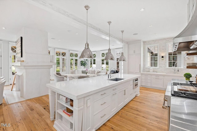 kitchen featuring sink, light wood-type flooring, an island with sink, pendant lighting, and white cabinets