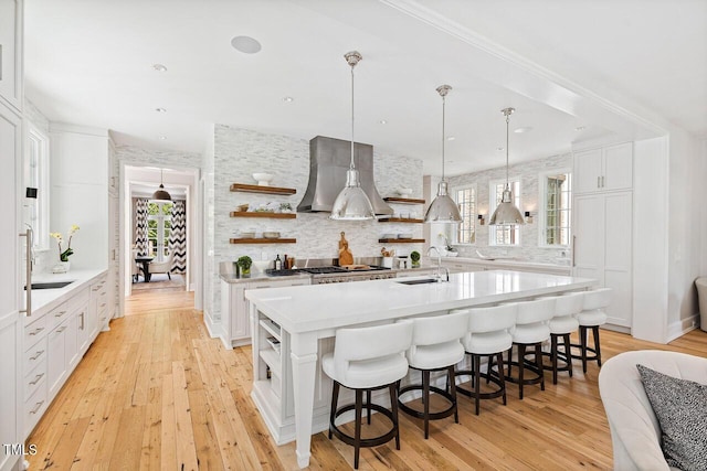 kitchen with sink, a center island with sink, white cabinets, and wall chimney exhaust hood