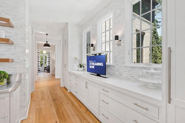 bar featuring white cabinetry, decorative backsplash, hanging light fixtures, and light wood-type flooring