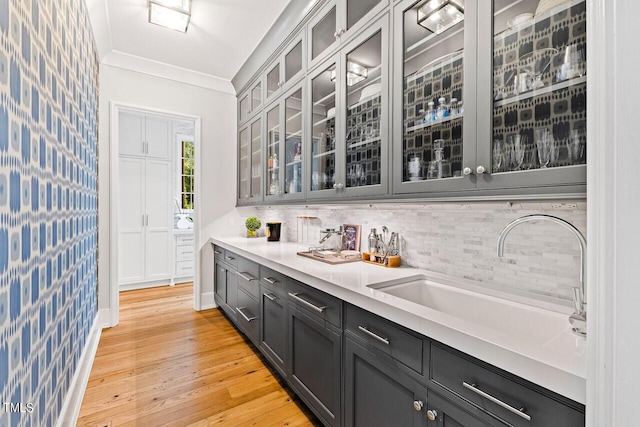 bar with ornamental molding, sink, backsplash, and light hardwood / wood-style flooring