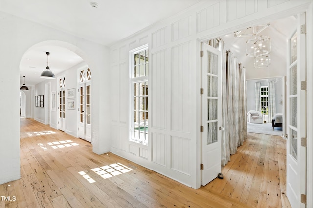 hallway with a notable chandelier, french doors, and light wood-type flooring