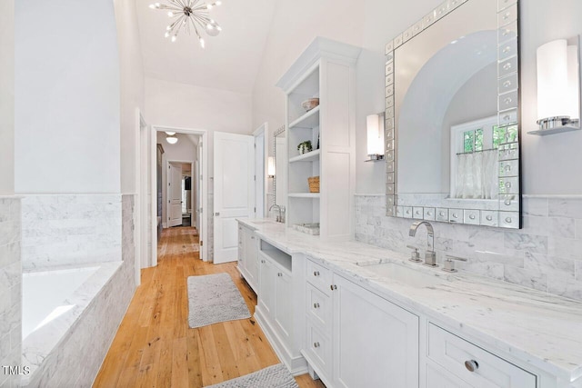 bathroom with wood-type flooring, a chandelier, decorative backsplash, vanity, and tiled tub