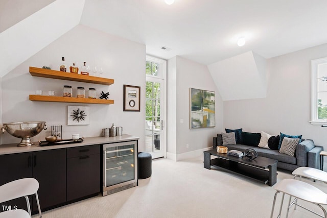 living room with wine cooler, lofted ceiling, light colored carpet, and bar area