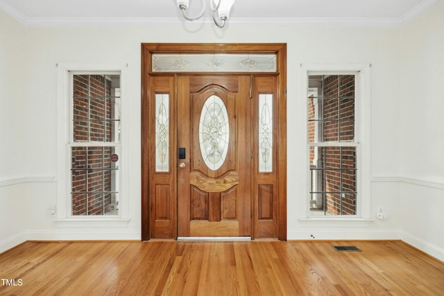 entrance foyer with ornamental molding, a chandelier, and light wood-type flooring