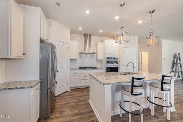 kitchen featuring wall chimney exhaust hood, sink, white cabinetry, decorative light fixtures, and stainless steel appliances