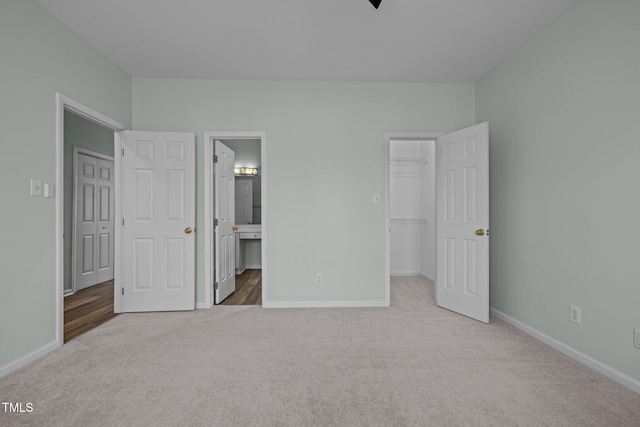 unfurnished bedroom featuring light carpet, a spacious closet, ensuite bath, and a closet