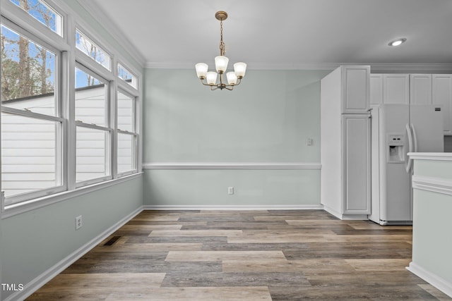 unfurnished dining area featuring ornamental molding, hardwood / wood-style floors, and an inviting chandelier