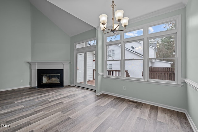 unfurnished living room with an inviting chandelier, a wealth of natural light, wood-type flooring, and vaulted ceiling