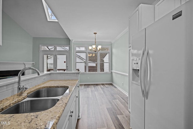 kitchen featuring sink, hanging light fixtures, a wealth of natural light, white fridge with ice dispenser, and white cabinets