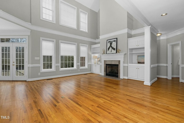 unfurnished living room featuring crown molding, light hardwood / wood-style flooring, a tile fireplace, built in shelves, and french doors