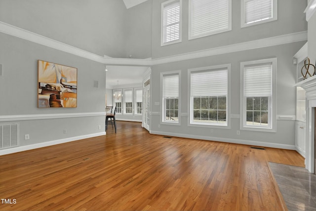 unfurnished living room featuring hardwood / wood-style floors, crown molding, a fireplace, and a high ceiling