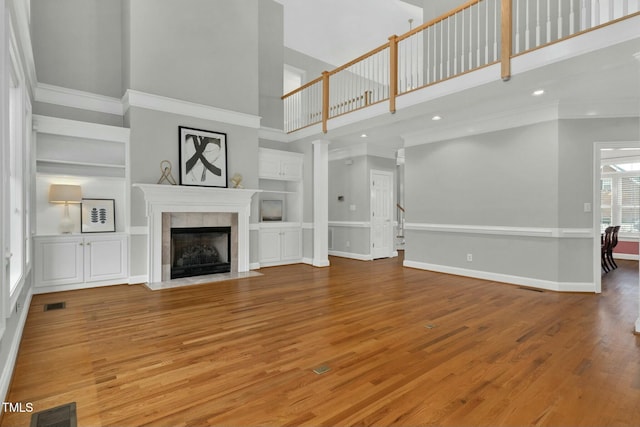 unfurnished living room with a tiled fireplace, hardwood / wood-style flooring, crown molding, and built in shelves