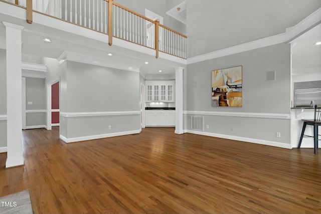 unfurnished living room featuring crown molding, wood-type flooring, a high ceiling, and ornate columns