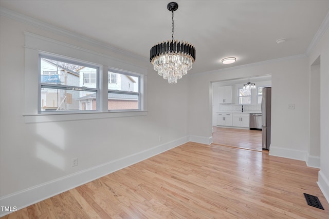 unfurnished dining area with light hardwood / wood-style flooring, ornamental molding, a chandelier, and plenty of natural light