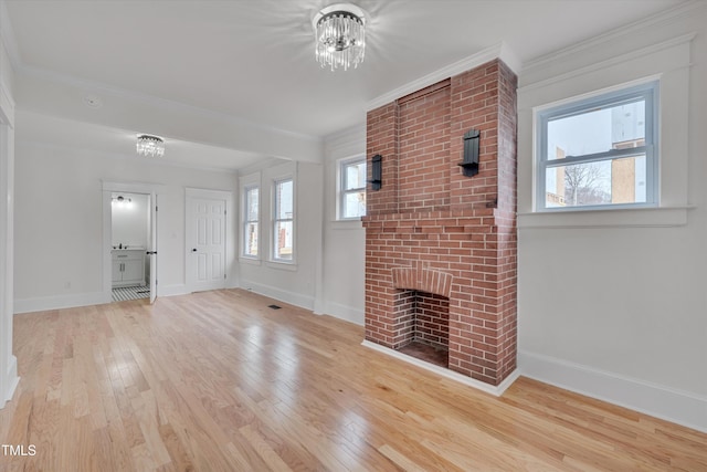 unfurnished living room with crown molding, a fireplace, a chandelier, and light wood-type flooring