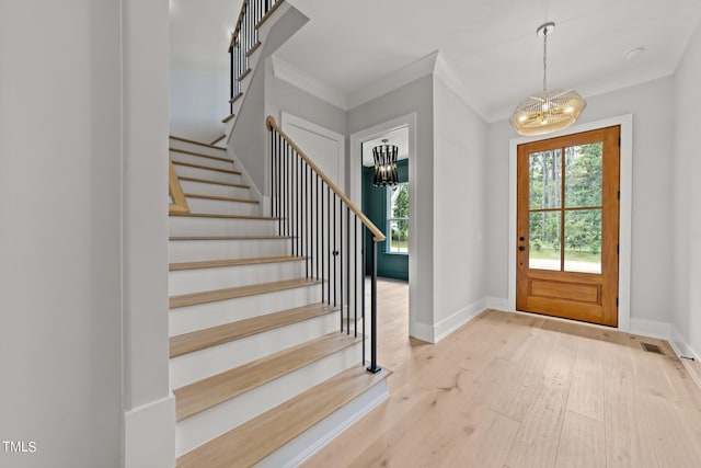 foyer with an inviting chandelier, ornamental molding, and light hardwood / wood-style floors