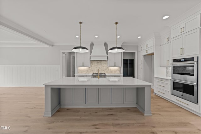 kitchen with a large island, double oven, custom exhaust hood, and hanging light fixtures