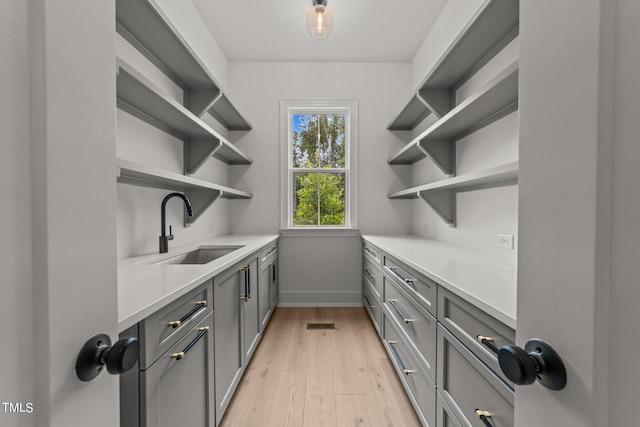 bar featuring sink, gray cabinets, and light hardwood / wood-style floors