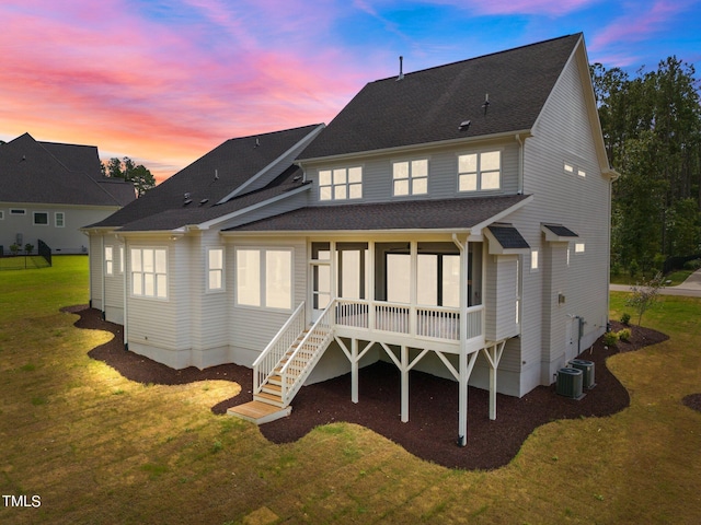 back house at dusk featuring a sunroom, a lawn, and central air condition unit