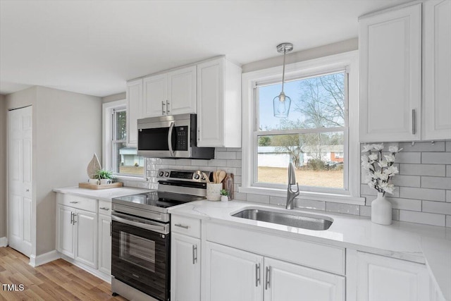 kitchen with sink, appliances with stainless steel finishes, hanging light fixtures, a wealth of natural light, and white cabinets