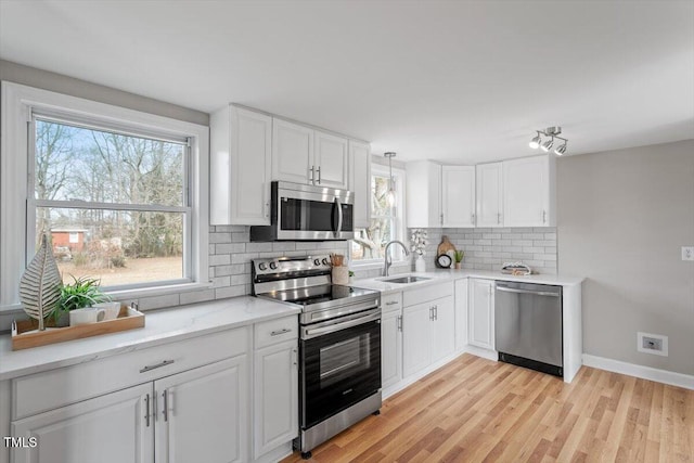 kitchen with sink, white cabinetry, hanging light fixtures, stainless steel appliances, and tasteful backsplash