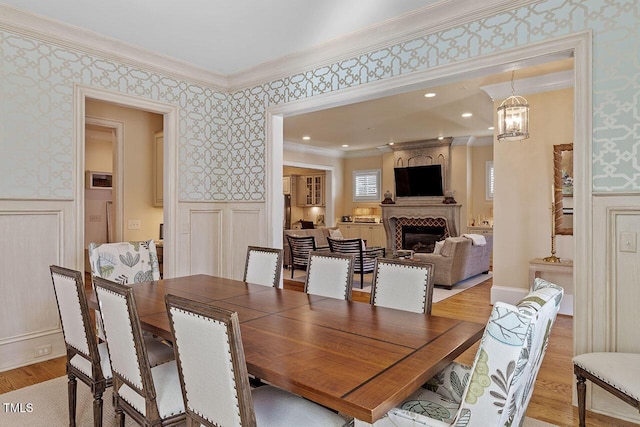 dining space with ornamental molding, a large fireplace, and light hardwood / wood-style floors