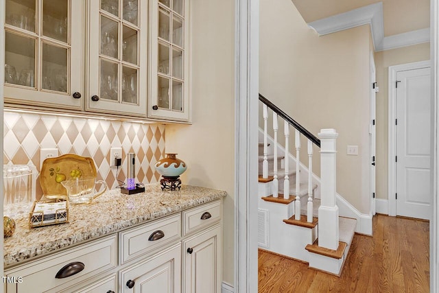 bar with ornamental molding, light stone countertops, backsplash, and light wood-type flooring