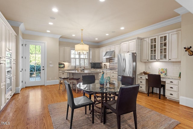 dining room with crown molding, built in desk, and light wood-type flooring