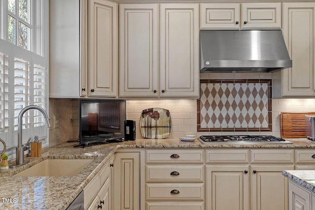 kitchen with stainless steel gas stovetop, sink, light stone counters, and decorative backsplash