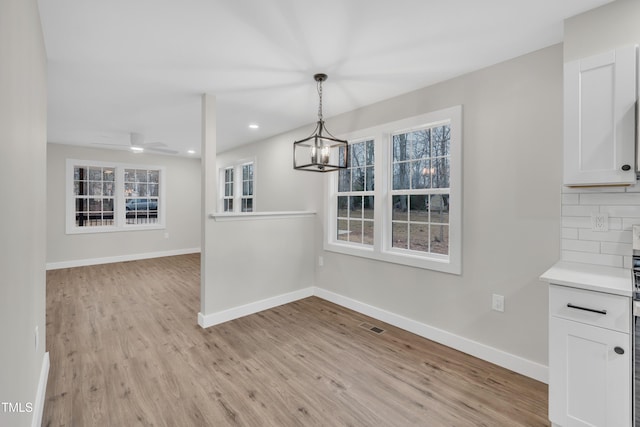 unfurnished dining area featuring ceiling fan with notable chandelier and light hardwood / wood-style flooring