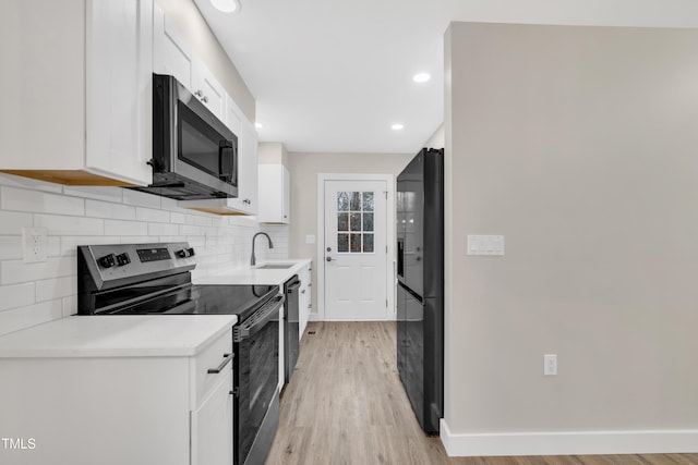 kitchen featuring sink, white cabinetry, black appliances, light hardwood / wood-style floors, and decorative backsplash