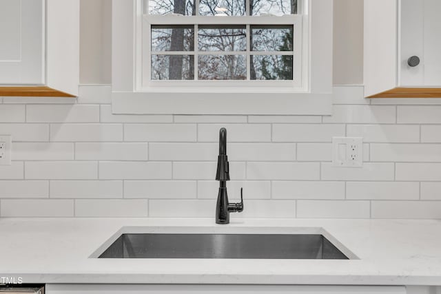 interior details featuring tasteful backsplash, sink, light stone countertops, and white cabinets